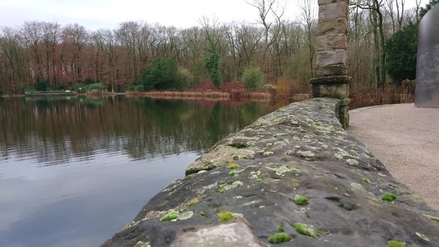Historic stone monument with trees and pond water in the background