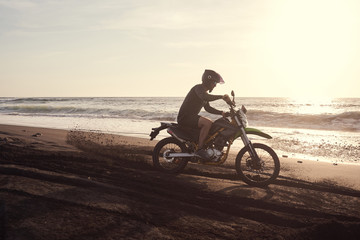 Fototapeta premium Male masculine model with cross road motorbike at the ocean coast with black sand at the golden hour time