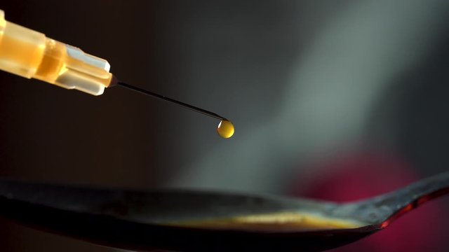 Droplets of Heroin from hypodermic needle syringe and spoon isolated in dimly lit area