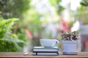 White coffee cup and pink flower with plant on wooden table at outdoor