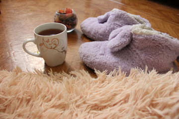 a pair of slippers on the floor next to a mug of tea and a fluffy plaid