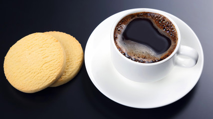 white cup of black coffee with biscuits on a dark background