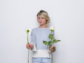 Portrait of young blonde beautiful woman with makeup in natural casual dress choosing between two flowers