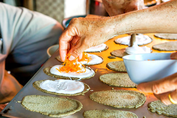 Old man's hand is making sweets Thai Crispy Pancake for customers. In picture he putting golden threads dessert on top of sweet cream and dough sheets.