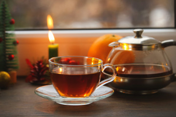 tea in a glass mug, a burning candle and Christmas decorations on the windowsill.