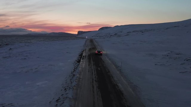 A supercar driving in a winter landscape during the winter. Aerial follow shot taken at the Nordkapp, Norway.