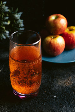Red apple soda on a dark table with apples in the background. Apple juice