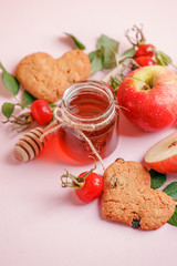 Ingredinets for winter fall autumn seasonal beverage tea party - fresh rose hip berries, honey, apple and heart-shaped biscuits. Concept of cozy teaparty witn immunity drink