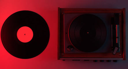 Retro vinyl record player with vinyl plates. Red neon light, top view