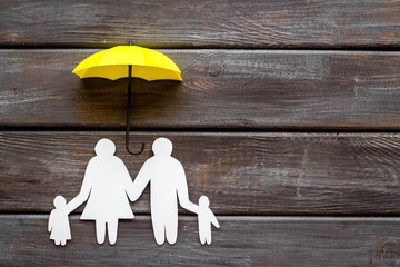Health insurance concept. Family cutout under umbrella on dark wooden background top-down copy space