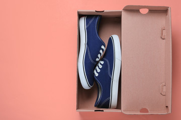 New fashionable sneakers and empty cardboard box on pink background. Top view