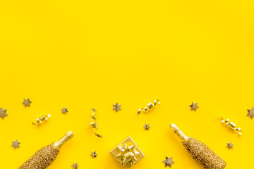 New Year background. Golden composition with champagne bottle and decorations on yellow desk top-down frame copy space