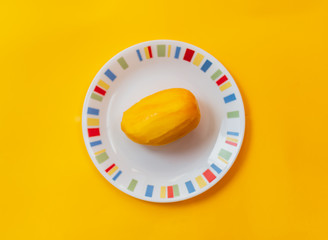One peeled mango fruit on a white plate kept on a yellow background. Single fresh mango without skin isolated icon with solid color backdrop. Skinless uncut whole fruit flat lay layout template.