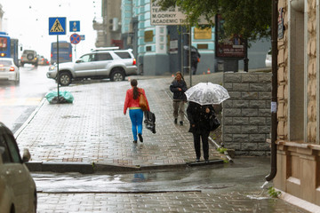 Rainy weather in the city. People walk under umbrellas during light rain on the wet streets of the city.