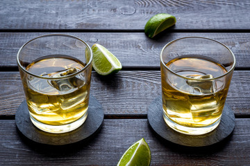 Whiskey with ice. To glasses of strong alcohol drink near lime on dark wooden background