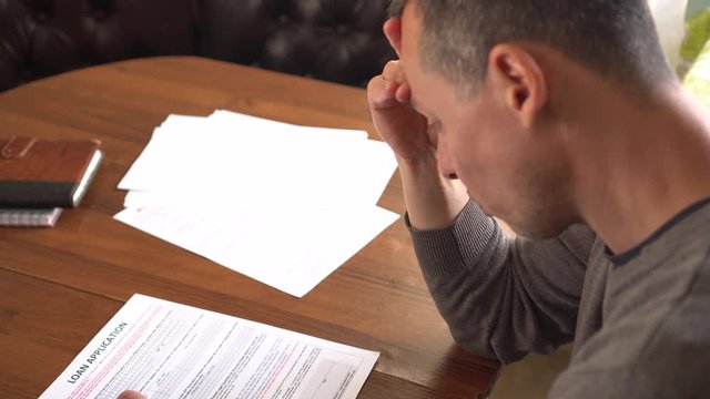 Unhappy sad man reading loan agreement. Loan application paper form 