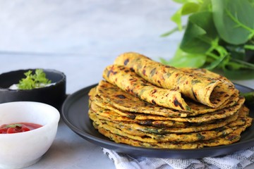 A Food called Methi paratha or Methi thepla is a Indian breakfast dish served with curd and ketchup. with copy space.