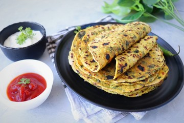 A Food called Methi paratha or Methi thepla is a Indian breakfast dish served with curd and ketchup. with copy space.