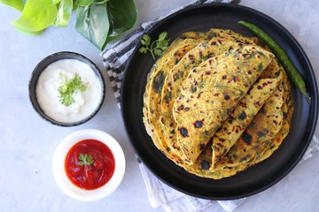A Food called Methi paratha or Methi thepla is a Indian breakfast dish served with curd and ketchup. with copy space.