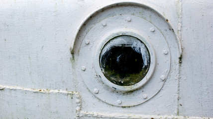 round porthole on board a white metal old ship