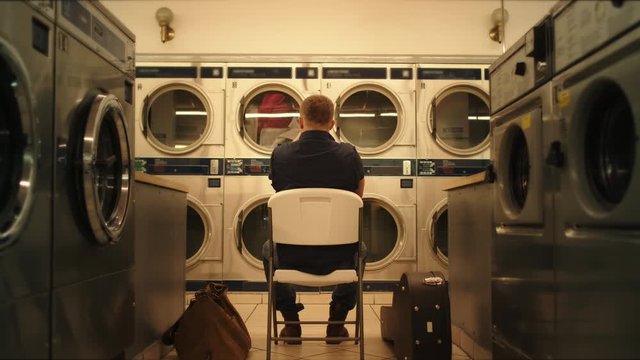 Man sits in laundry and waits clothes to wash, moment from everyday life, washing machines
