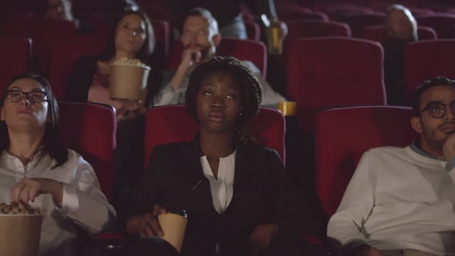 Tracking shot of multi-ethnic audience watching movie in dark cinema. Unrecognizable people standing up from their seats and leaving