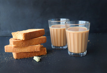Tea Time Food - Healthy Wheat rusk served with Indian hot cardamom flavored or masala tea, over black background with whole cardamom. Copy space
