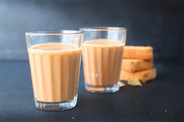 Tea Time Food - Healthy Wheat rusk served with Indian hot cardamom flavored or masala tea, over black background with whole cardamom. Copy space