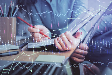 A woman hands writing information about stock market in notepad. Forex chart holograms in front. Concept of research. Multi exposure