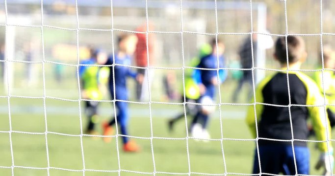 Soccer match of small soccer players. Kids playing soccer match at outdoor playground. Intentionally focused on the gate net. Players in the background intentionally out of focus.