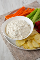 Homemade Caramelized Onion Dip with Potato Chips, Celery, Pepper and Carrot on a white wooden table, low angle view. Close-up.