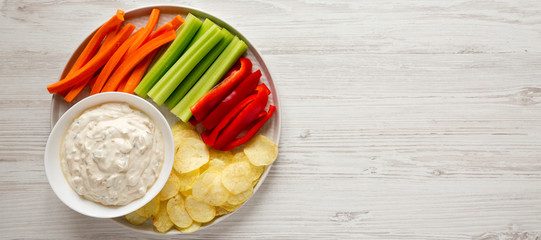 Obraz na płótnie Canvas Homemade Caramelized Onion Dip with Potato Chips, Celery, Pepper and Carrot on a white wooden surface, top view. Flat lay, overhead, from above. Copy space.