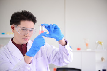 Asian chemist looking at beaker in laboratory and doing research..