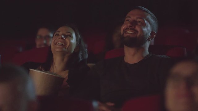 Medium shot of happy young woman and man laughing while watching funny movie in theater