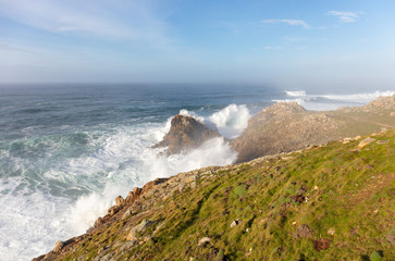 Big waves on the high cliffs of the Spanish Atlantic coast. The waves are very high and roll over. There is a haze in the air. The exciting coast in Galicia in northern Spain.