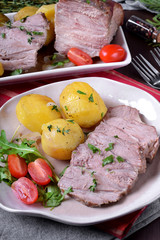 Roasted pork meat cut into slices served with potato, tomato and arugula on the white ceramic plate. Festive meal