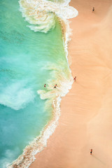 View from above, stunning aerial view of some tourists playing, sunbathing and swimming on a beautiful beach bathed by a turquoise sea during sunset. Kelingking beach, Nusa Penida, Indonesia.