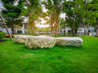 The white stone decorated on fresh green Burmuda grass smooth lawn as a carpet, bush and trees on the background, good maintenance landscapes in garden under morning sunlight