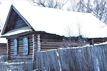 An old, wooden, log house, the roof of which is covered with snow.