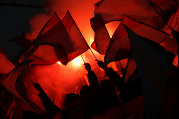 Silhouettes of sport fans holding flags with red pyrotechnical light in the background