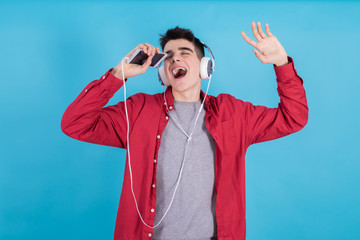 young teenage man singing with mobile phone and headphones isolated on blue background