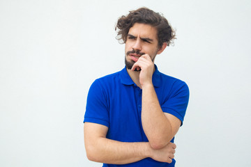 Pensive focused guy biting nails and fingers, staring away. Handsome bearded young man in blue casual t-shirt posing isolated over white background. Thinking concept