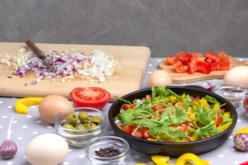 Set of vegetables for healthy eating, yellow and red peppers, olives, tomatoes, onions, garlic. Sliced vegetables in pan. Knife and onions on cutting board. Top view. .