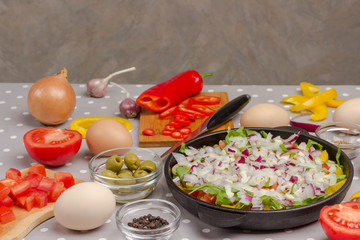 Set of vegetables for a healthy eating, yellow and red peppers, olives, tomatoes, onions, garlic. Sliced vegetables in pan. Knife and pepper on cutting board. Top view. .