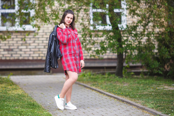 close up portrait of big plus size beautiful stylish kid girl with leather jacket  and red plaid shirt near brick building in urban street as background