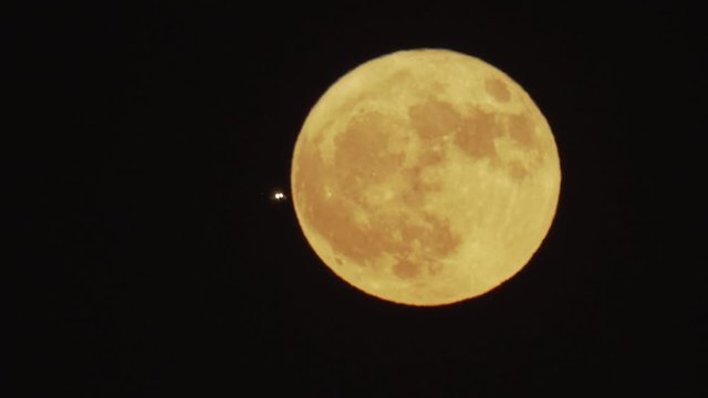 An airliner lines up for a nighttime final approach to Los Angeles International Airport in front of a full moon.