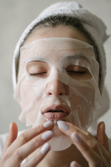Cosmetic natural face mask against aging and facial wrinkles. A young woman in a towel applies a mask to moisturize face
