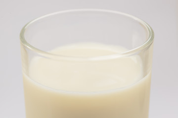 A cup of soy milk stands alone on a pale yellow background.