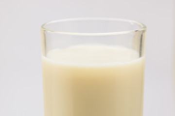 A cup of soy milk stands alone on a pale yellow background.