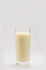 A cup of soy milk stands alone on a pale yellow background.